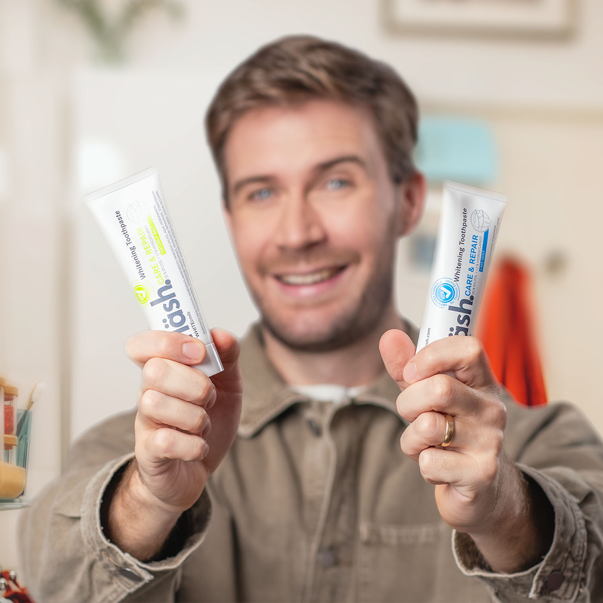 ein junger Mann in hellbraunem Cordhemd hält prominent 2 Tuben fläsh Zahnpasta in den in Richtung Kamera ausgestreckten Händen. Der Fokus der Kamera liegt auf den beiden Zahnpastatuben.