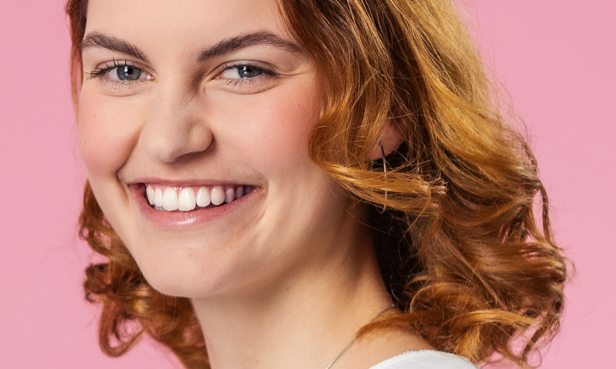 Eine junge, rothaarige Frau lächelt sympathisch in die Kamera. Ihre Zähne sind cremefarben, da sie noch kein professionelles Bleaching mit fläsh hatte.