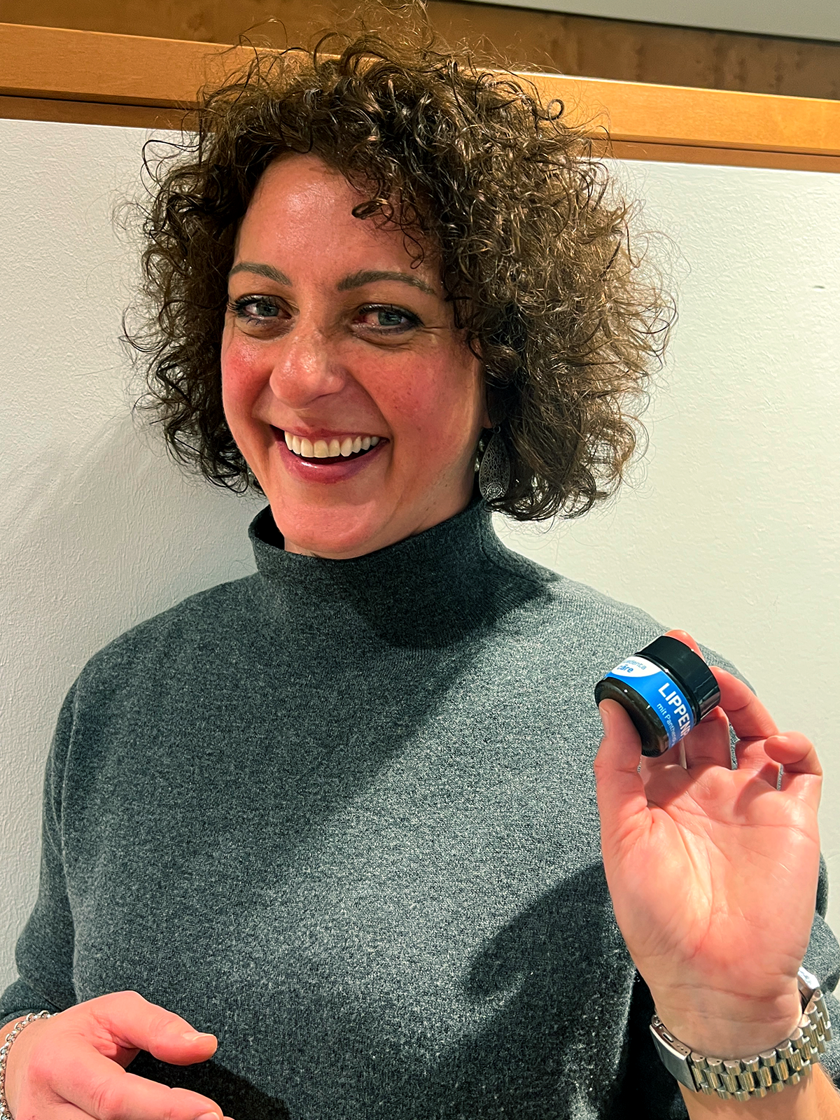 Zahnärztin Dr. Nadine Seitner empfiehlt mit einem Lächeln die bluedenta cäre Lippenpflege. Sie zeigt den blau gelabelten Glastiegel der Lippenpflege in die Kamera.