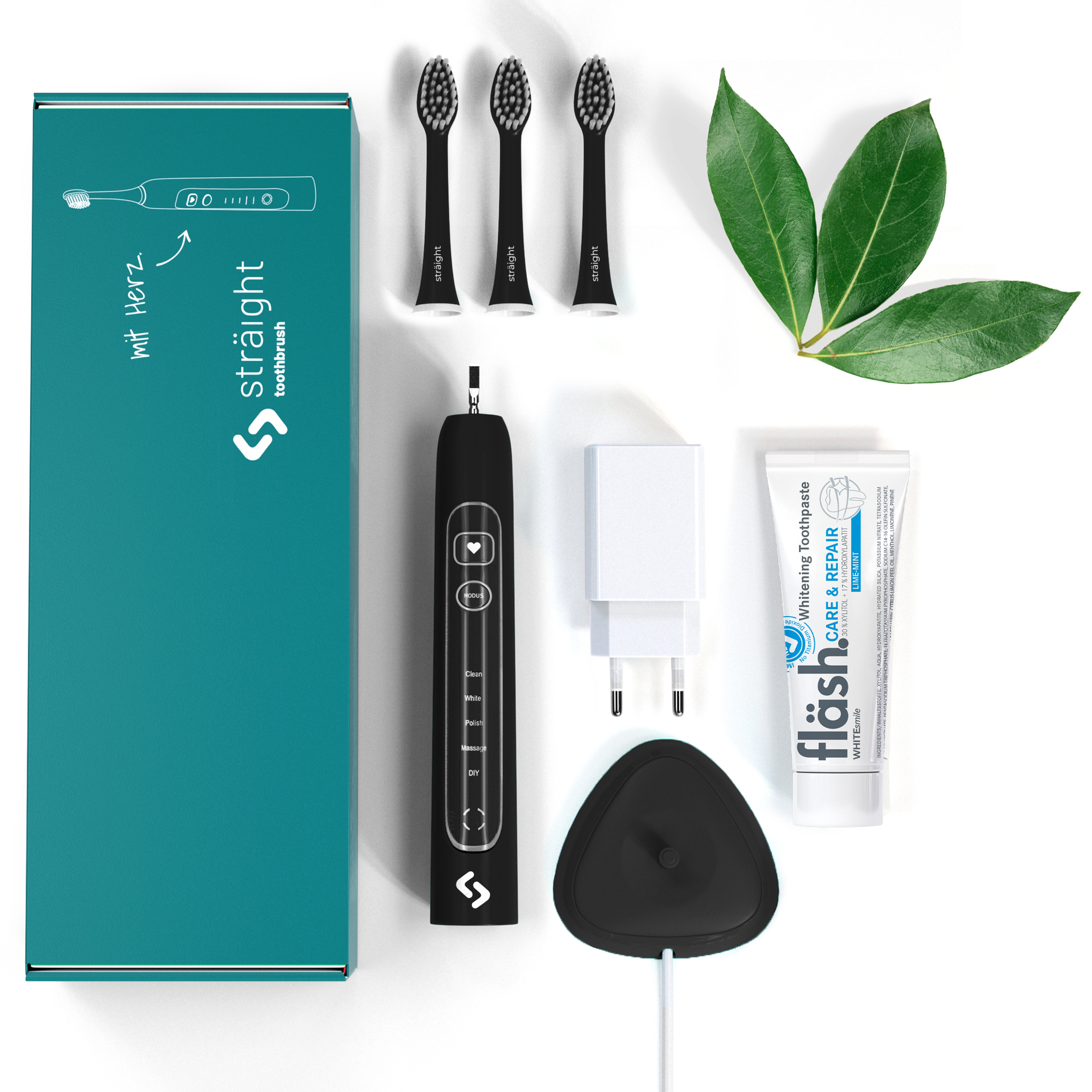 Auf weissem Hintergrund liegen alle im Lieferumfang enthaltenen Elemente der sträight Schallzahnbürste, Modell "schwarz": der grüne Produktkarton, 3 Bürstenköpfe, der Zahnbürstengriff, die Ladestation mit Stecker sowie eine Tube fläsh Zahnpasta.