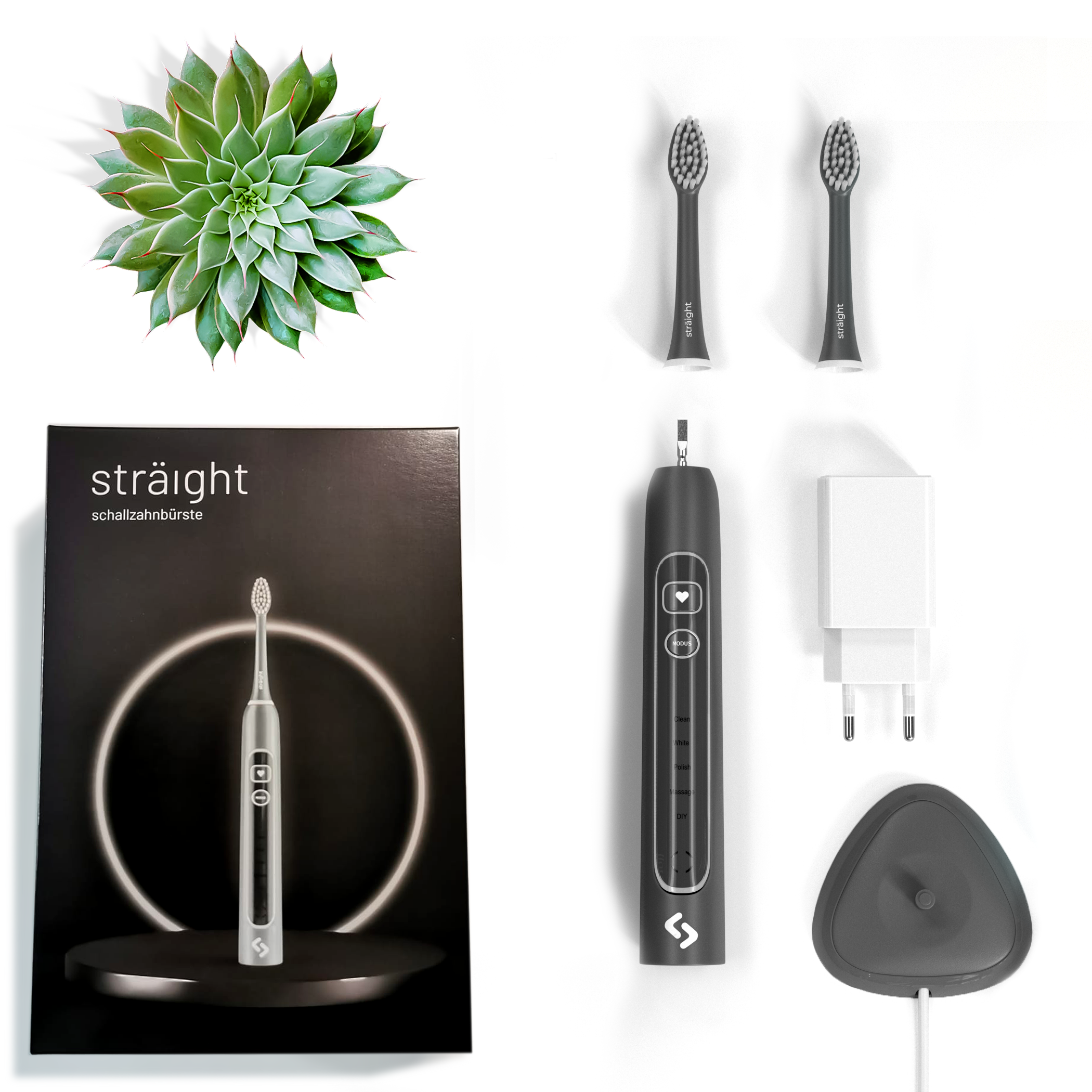 Auf weissem Hintergrund liegen alle im Lieferumfang enthaltenen Elemente der sträight Schallzahnbürste, Modell "Grau Light": der schwarze Produktkarton, 2 Bürstenköpfe, der Zahnbürstengriff, die Ladestation mit Stecker.