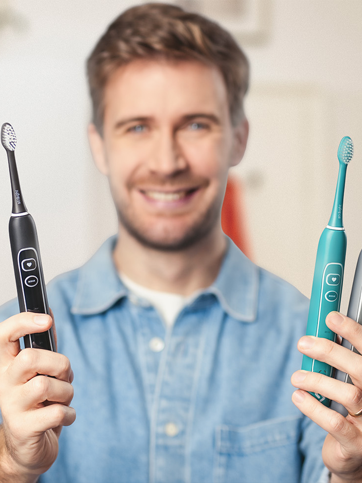 Ein junger Mann im Jeanshemd und mit sympathischem Lächeln hält in der rechten Hand eine schwarze, und in der linken Hand eine grüne sträight Schallzahnbürste dem Betrachter entgegen. 