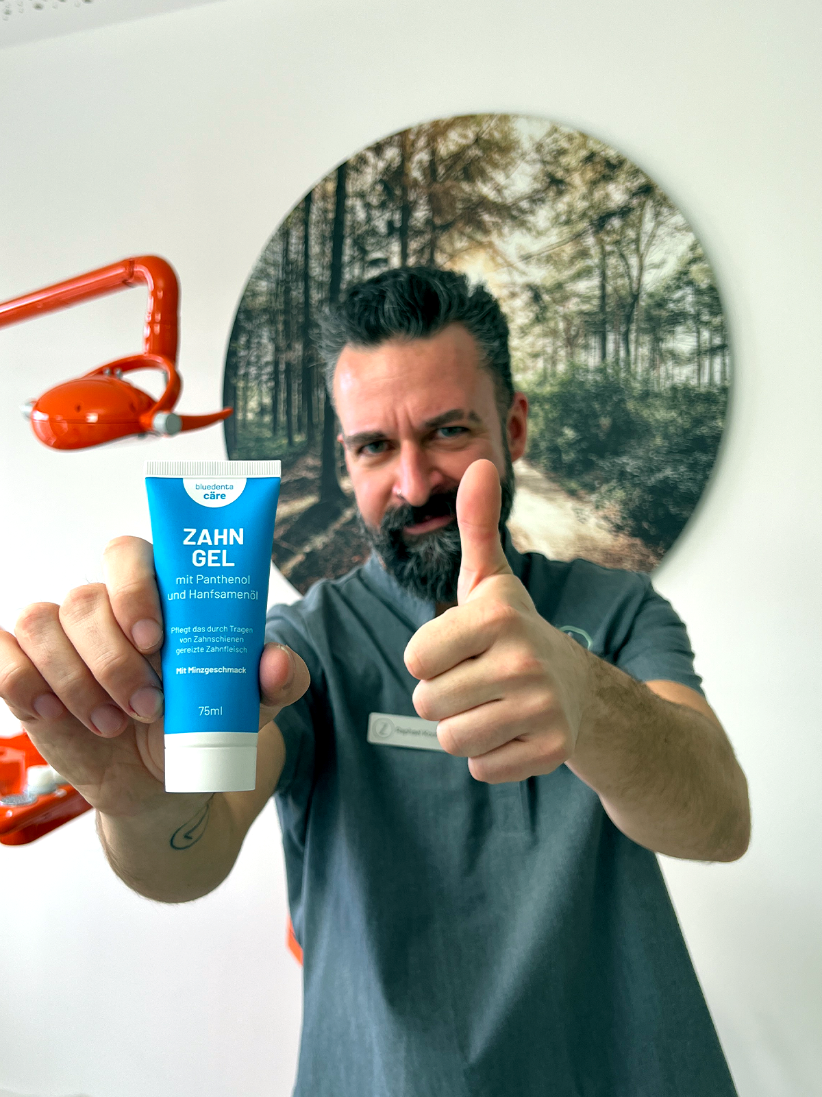 Im Behandlungsraum der Praxis Lindenthal in Köln. Dentalhygieniker Rapahael Koutelas gibt ein Daumen-Hoch-Zeichen für das Zahngel von bluedenta cäre. die dazugehörige himmelblaue Tube hält er in der rechten Hand prominent in die Kamera.