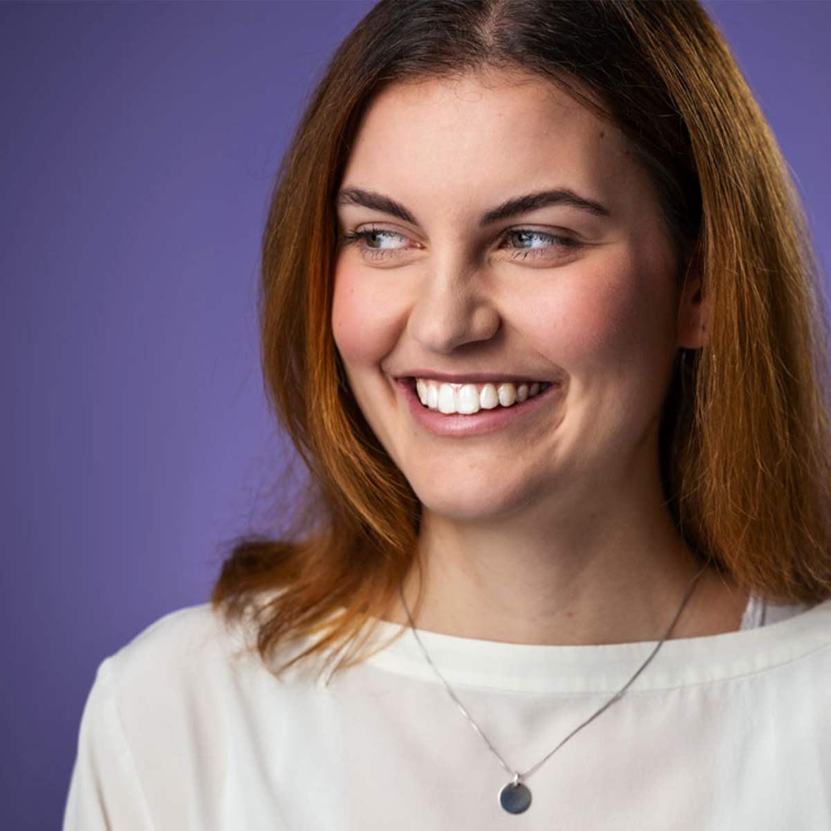 Eine rothaarige junge Frau schaut lächelnd zur Seite.